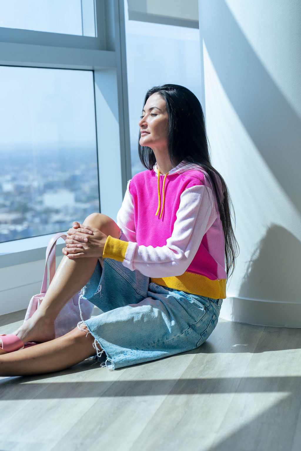 Woman sitting by a window with a cityscape view, wearing a color blocked sweater by Blythly