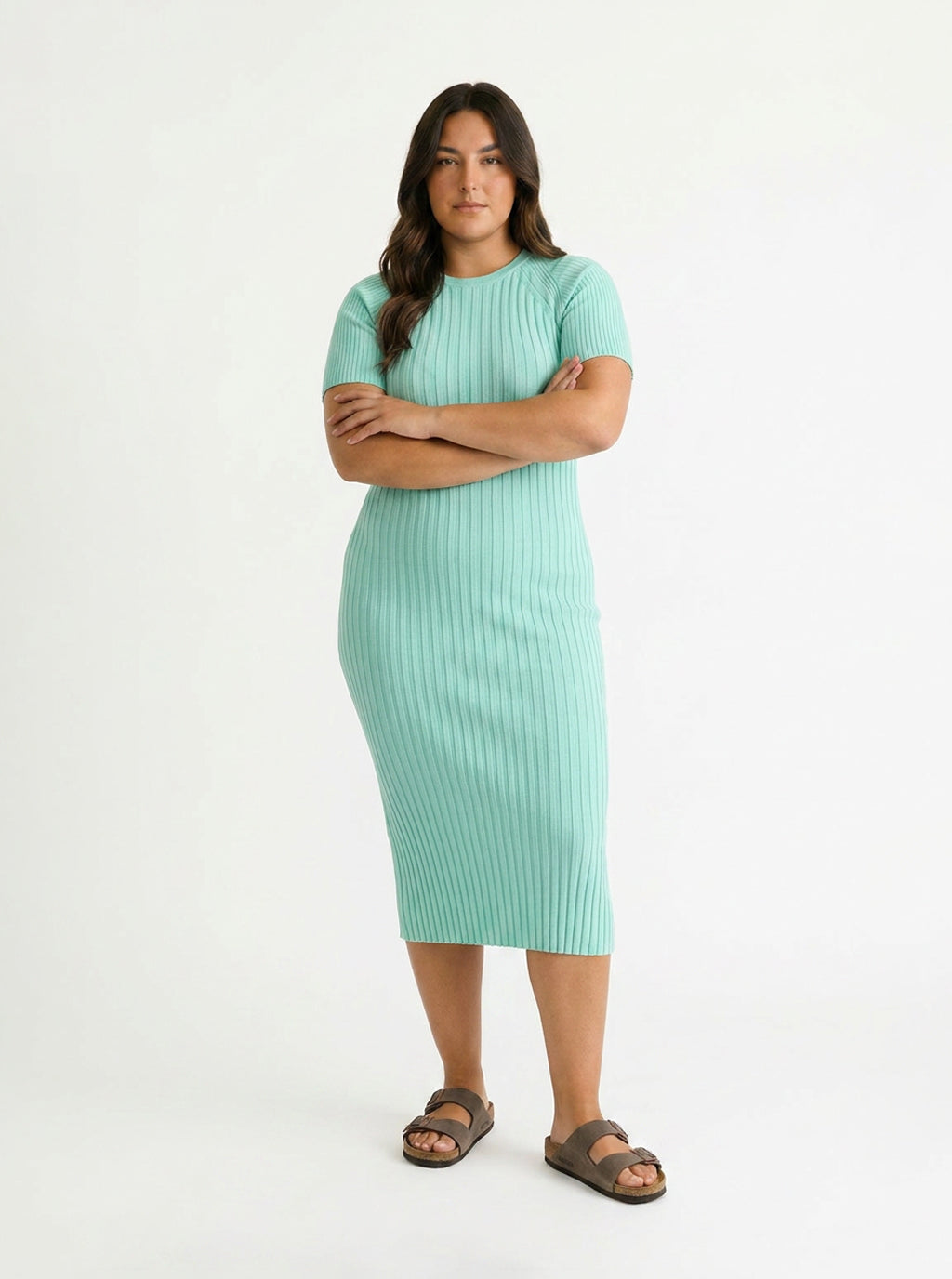 A woman modeling a mint green ribbed short-sleeve midi dress with brown slide sandals, standing against a plain white studio background.