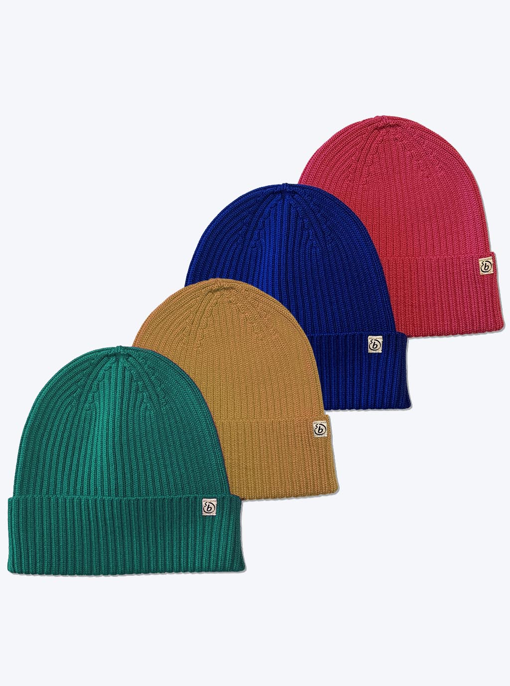 Four ribbed knit beanie hats in teal green, mustard yellow, royal blue, and magenta arranged in a diagonal stack on a light gray background. Each hat has a small square white logo patch on the cuff.